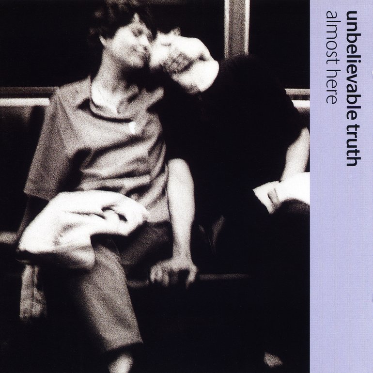 cover de l'album Almost Here du groupe Unbelievable truth. Il est compos&eacute; d'une photo en noir et blanc d'un homme et une femme assis c&ocirc;te &agrave; c&ocirc;te dans le m&eacute;tro. L'homme a la t&ecirc;te enfouie dans le cou de la femme, elle sourit, les yeux ferm&eacute;s. La photo est tr&egrave;s floue. Le nom du groupe et de l'album sont inscrits sur un bandeau violet sur le c&ocirc;t&eacute;.