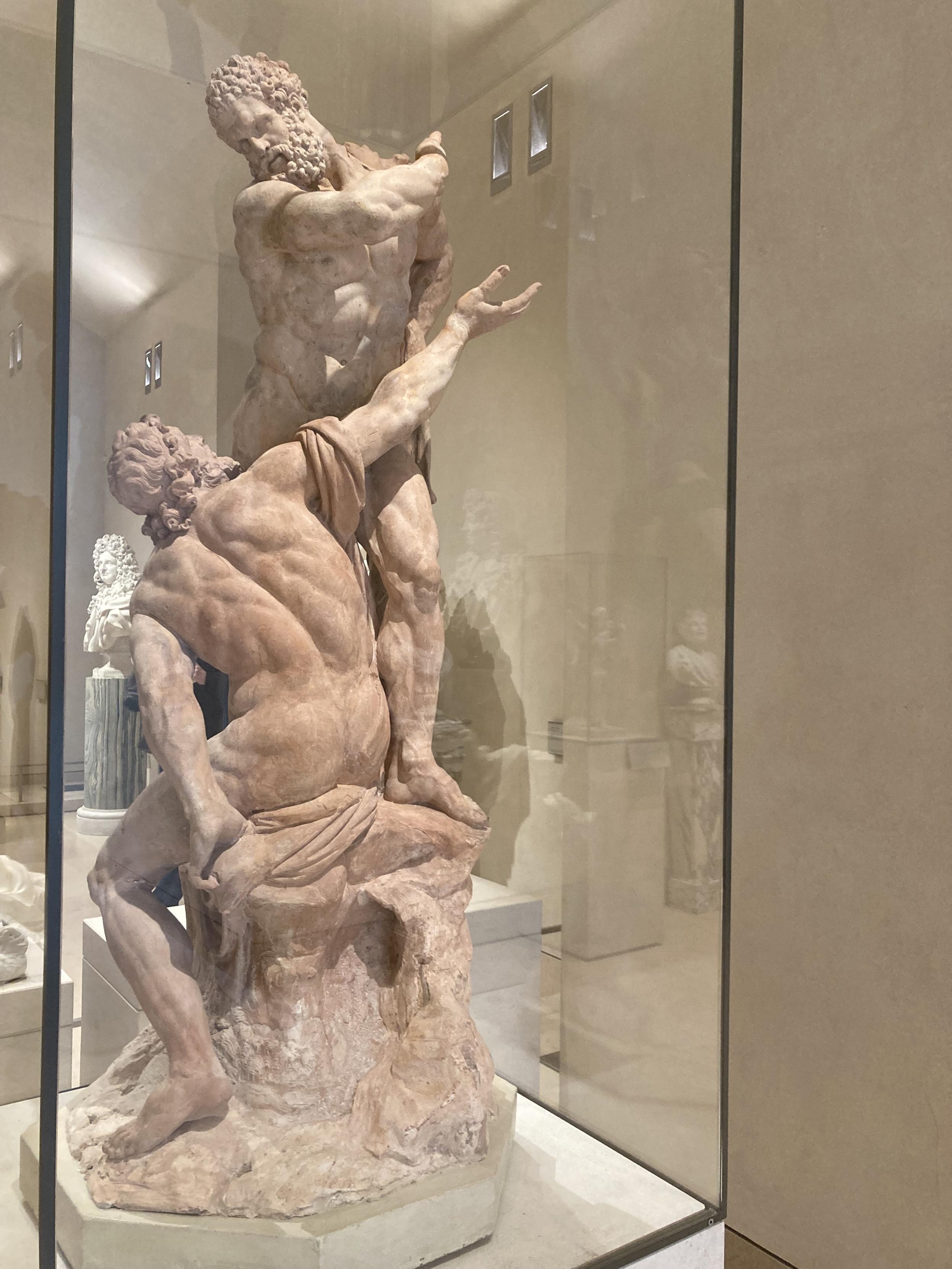 Sculpture de 2 hommes, l’un est assis, de dos et regarde l’autre, debout, qui arme son bras comme pour lui mettre une énorme gifle