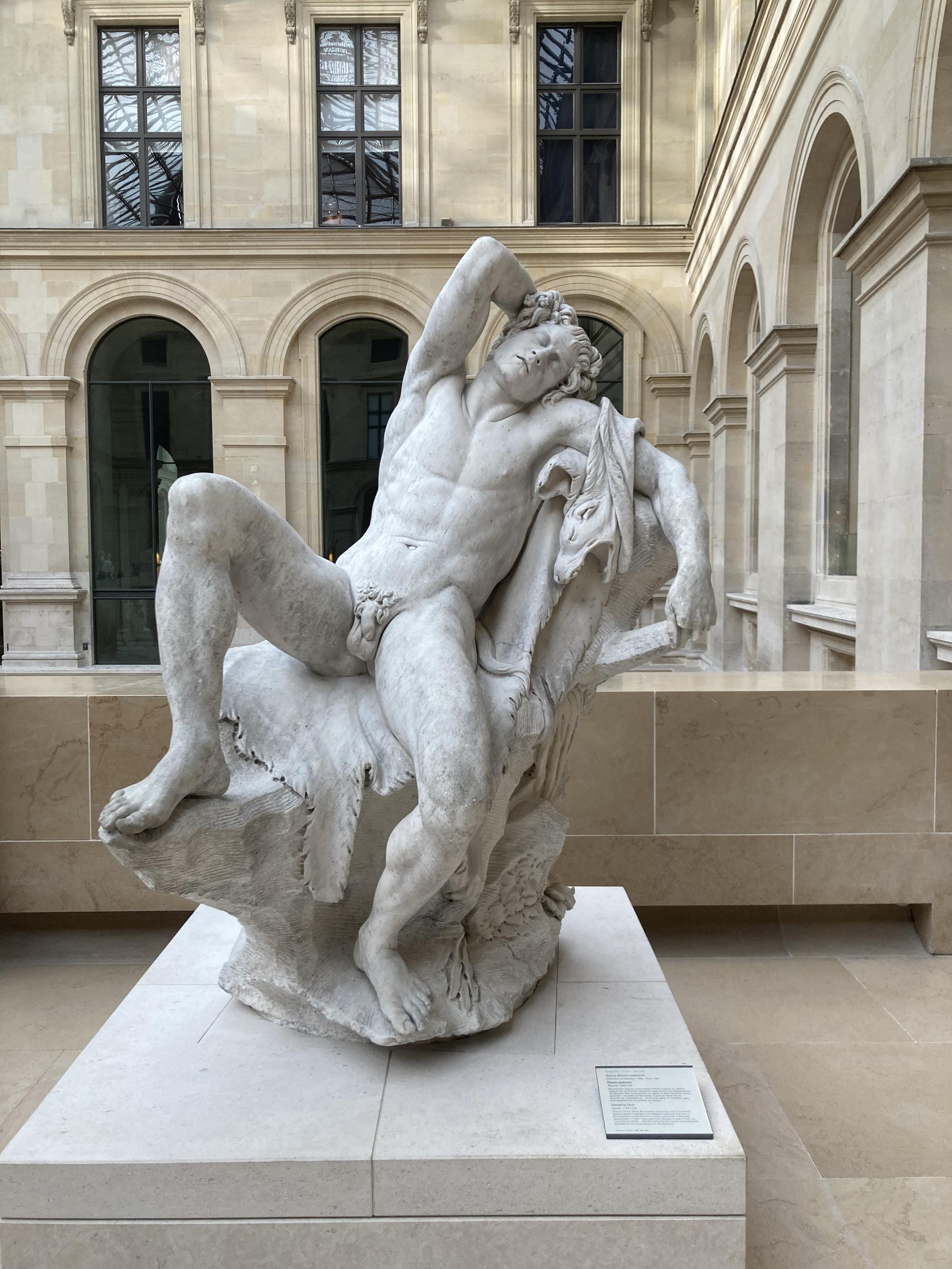Statue d’un homme nu, assis avec les jambes écartées et une main dans se cheveux, comme s’il voulait nous faire admirer à quel point il est bien foutu