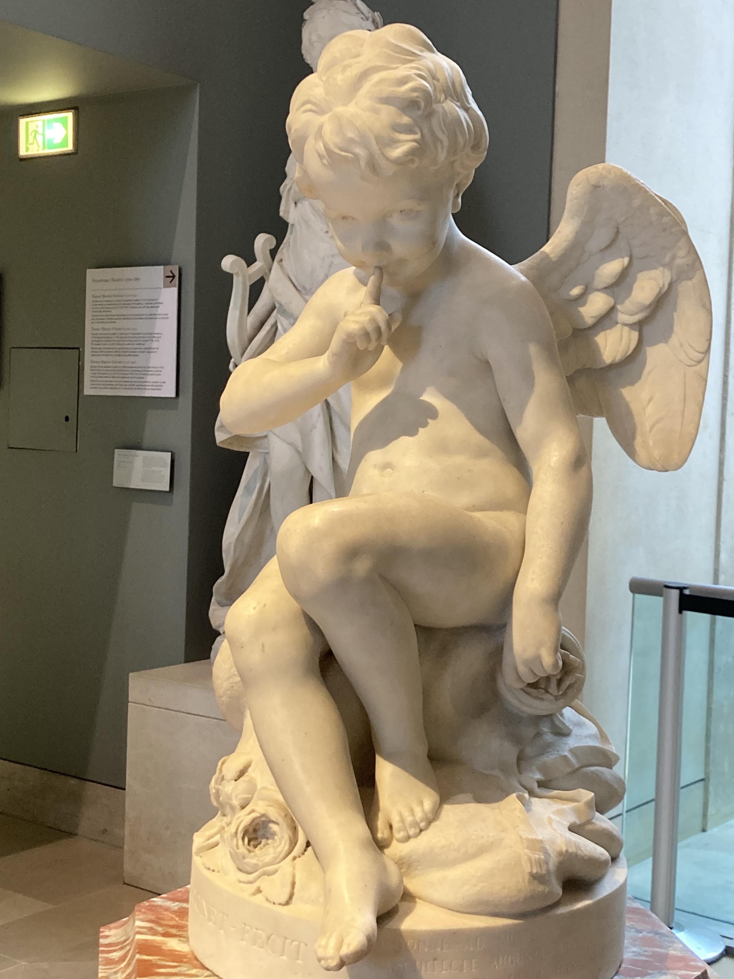 Statue d’un enfant assis, avec un doigt sur sa bouche et un air coquin