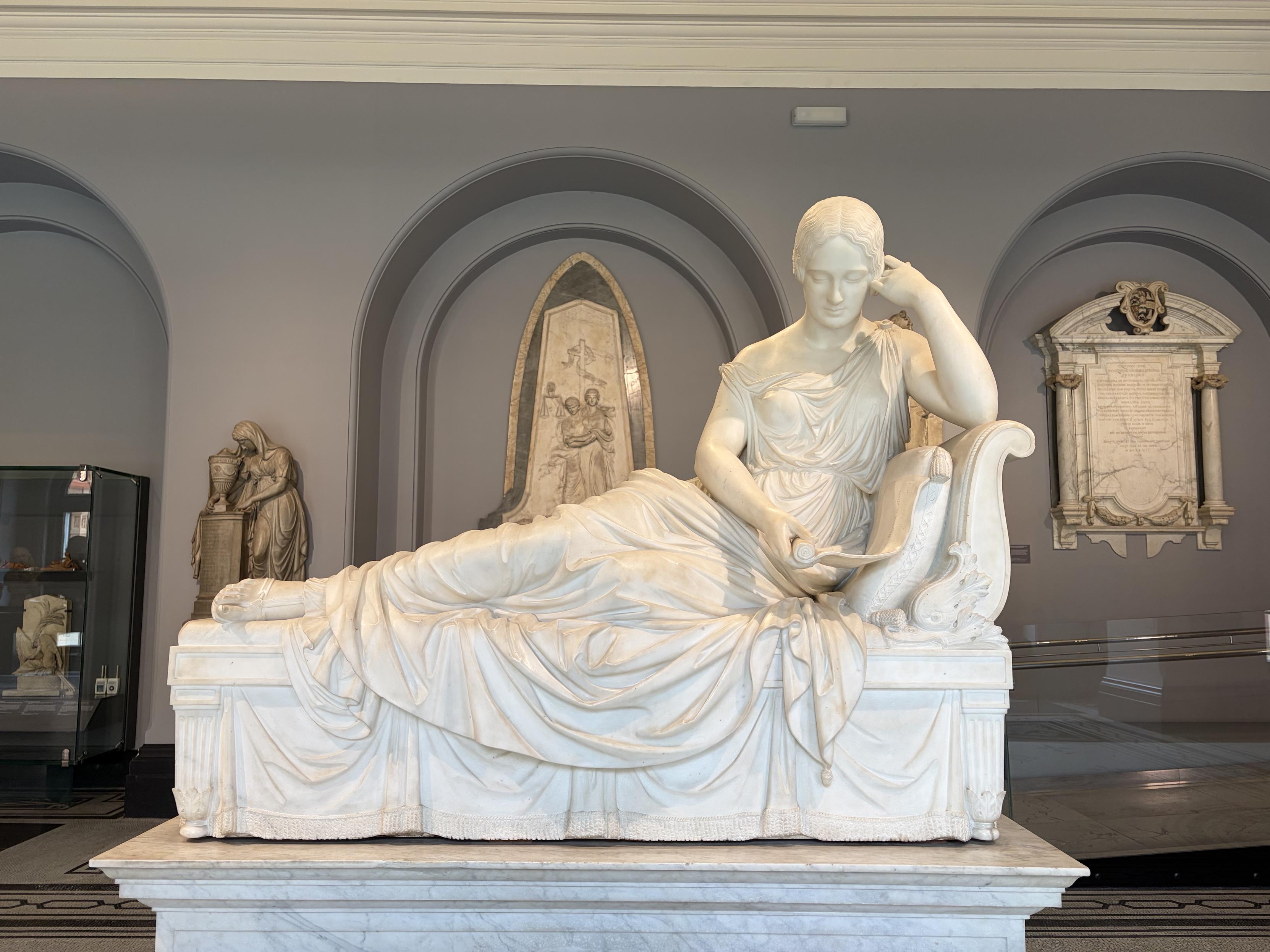 Sculpture d&rsquo;une jeune femme alanguie sur un si&egrave;ge, en train de lire un parchemin