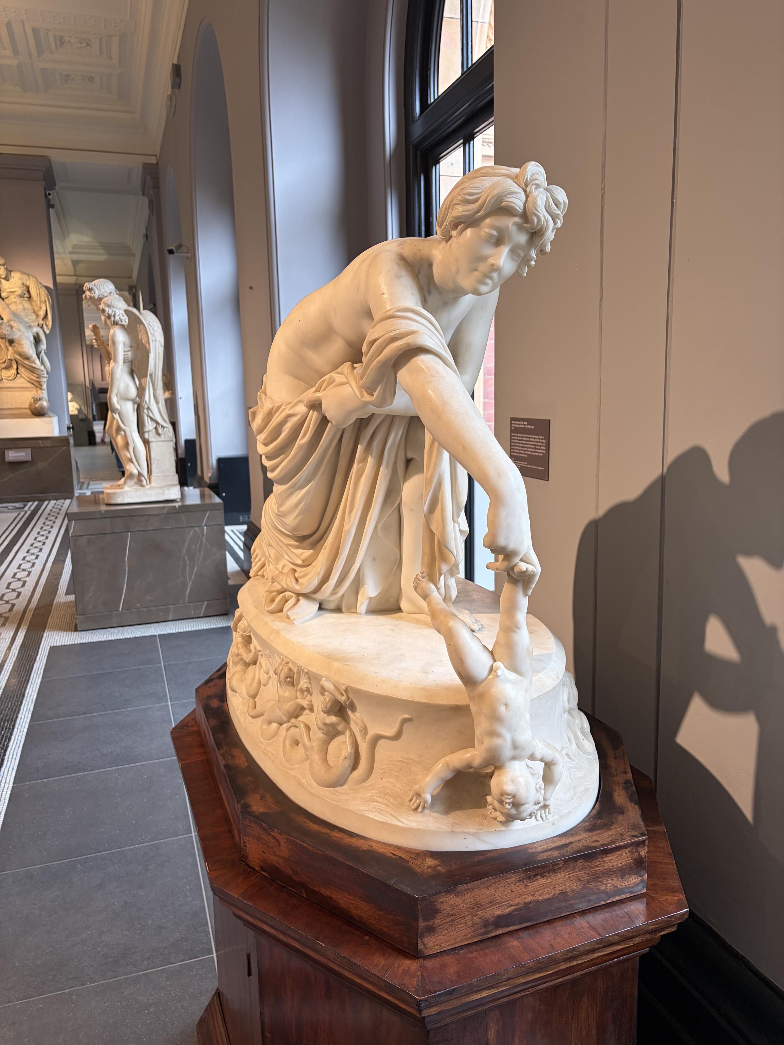 Sculpture d&rsquo;une m&egrave;re tenant son b&eacute;b&eacute; par la cheville, t&ecirc;te en bas